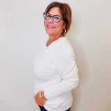 Woman wearing a white long sleeve top and blue jeans against a plain background