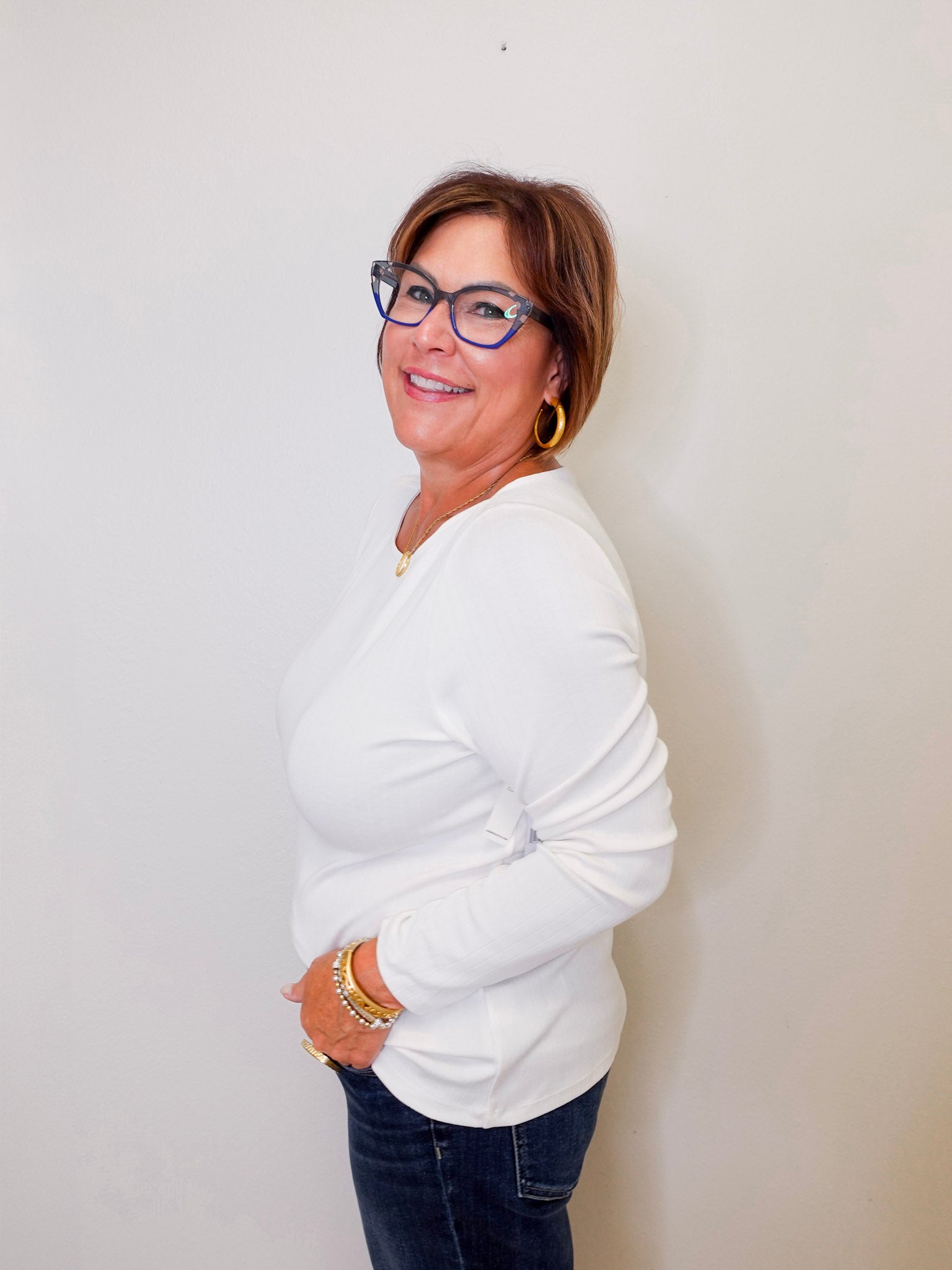 Woman wearing a white long sleeve top and blue jeans against a plain background