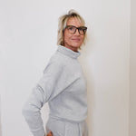 Woman wearing a gray outfit against a white wall