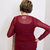 Person wearing a maroon long-sleeve top with mesh back panel against a white background