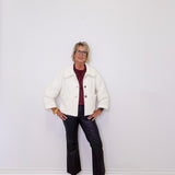 Person wearing a white jacket, red shirt, black pants, and pink shoes against a white wall.