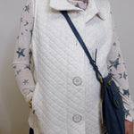 Person wearing a white quilted vest over a star-patterned shirt, holding a navy blue handbag.
