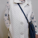 Person wearing a white quilted vest over a star-patterned shirt, holding a navy blue handbag.