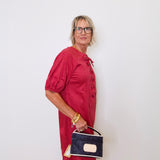 Woman in a red dress holding a black handbag against a white wall
