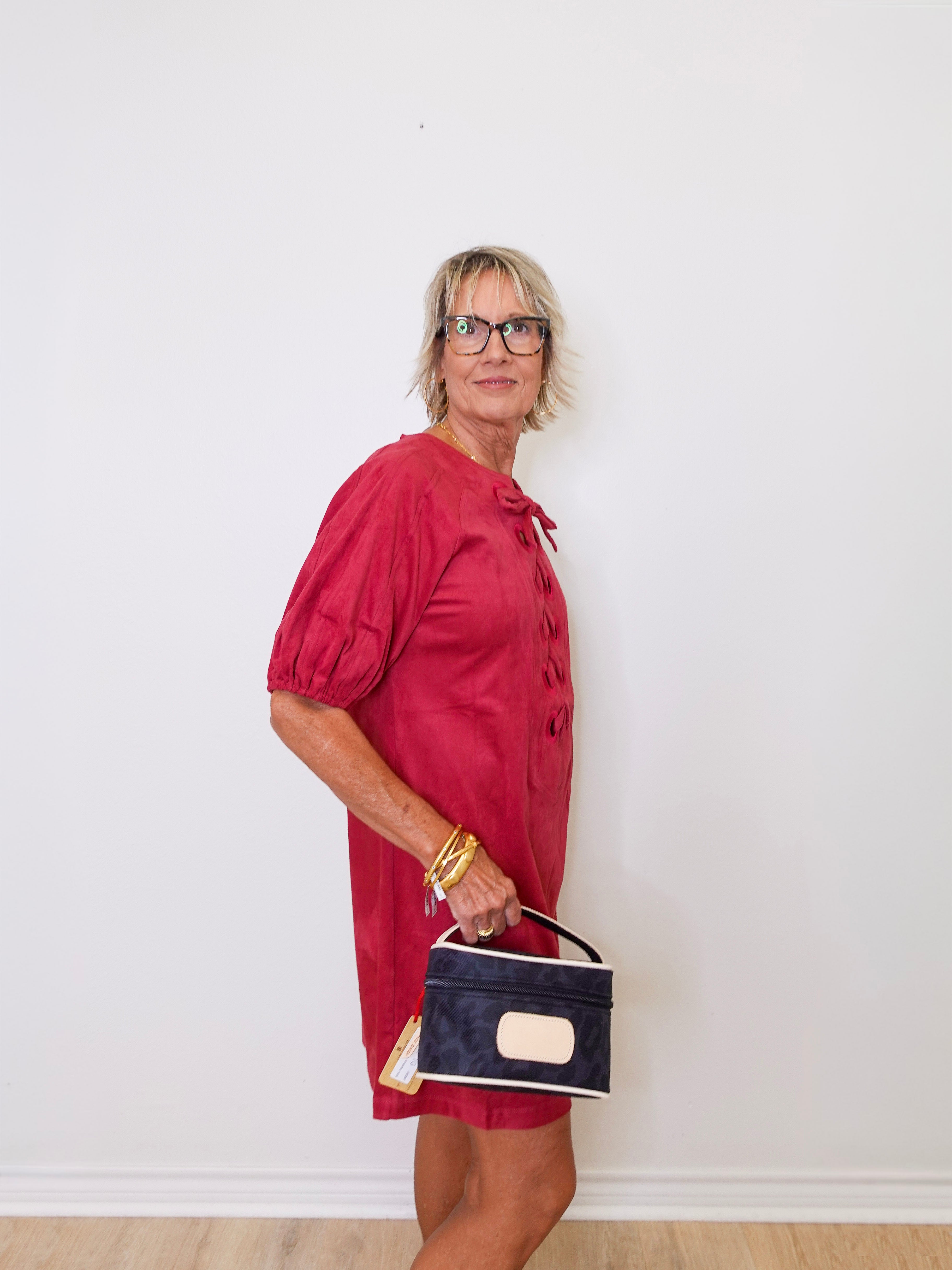 Woman in a red dress holding a black handbag against a white wall