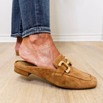 Brown suede loafer worn with blue jeans on a wooden floor.