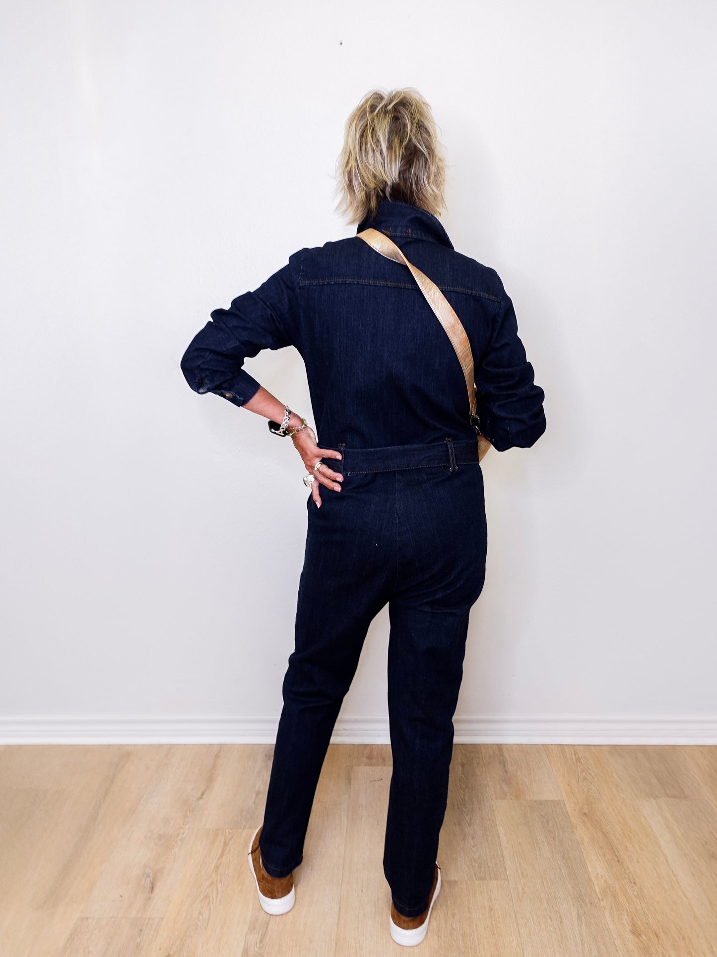 Person wearing a dark denim jumpsuit standing against a white wall.