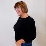 Woman wearing a black top and blue jeans against a white background
