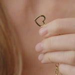 Gold heart-shaped earring held by a hand against a blurred background