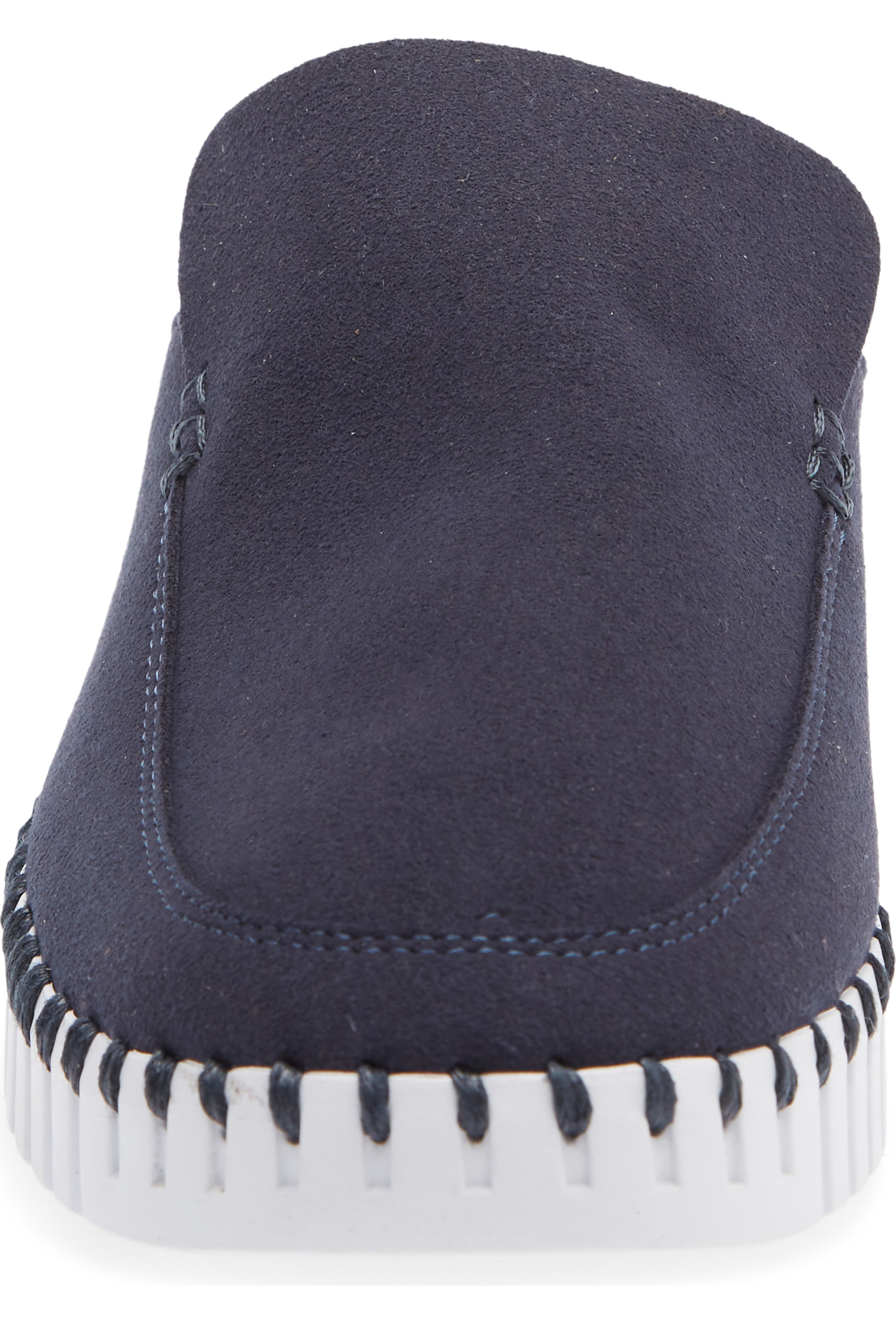A close-up rear view of a slip-on slipper in dark navy blue suede, featuring a white sole with black contrast stitching around the edge.