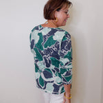Woman wearing a patterned shirt and white shorts against a plain background