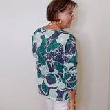 Woman wearing a patterned shirt and white shorts against a plain background