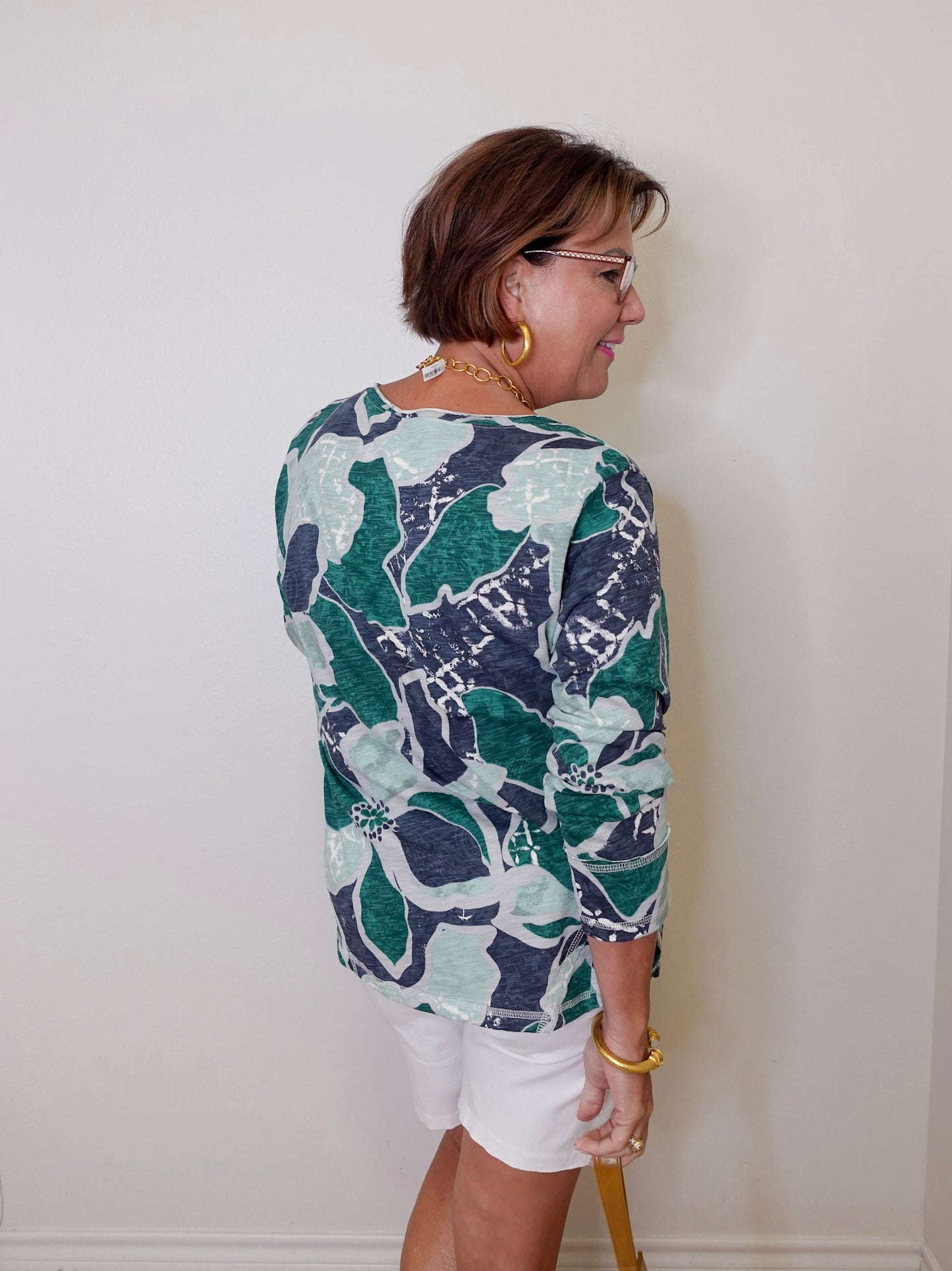 Woman wearing a patterned shirt and white shorts against a plain background