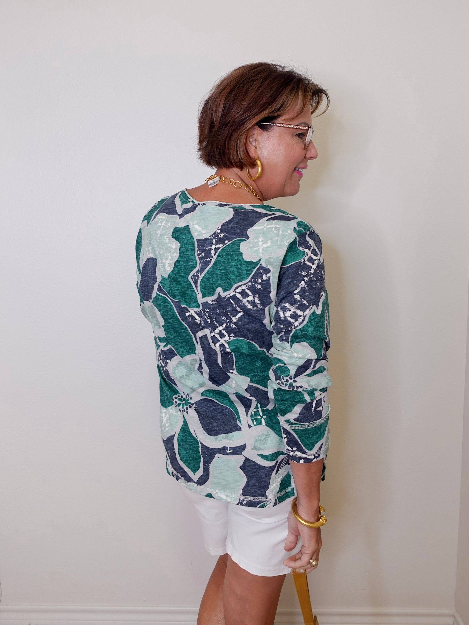Woman wearing a patterned shirt and white shorts against a plain background