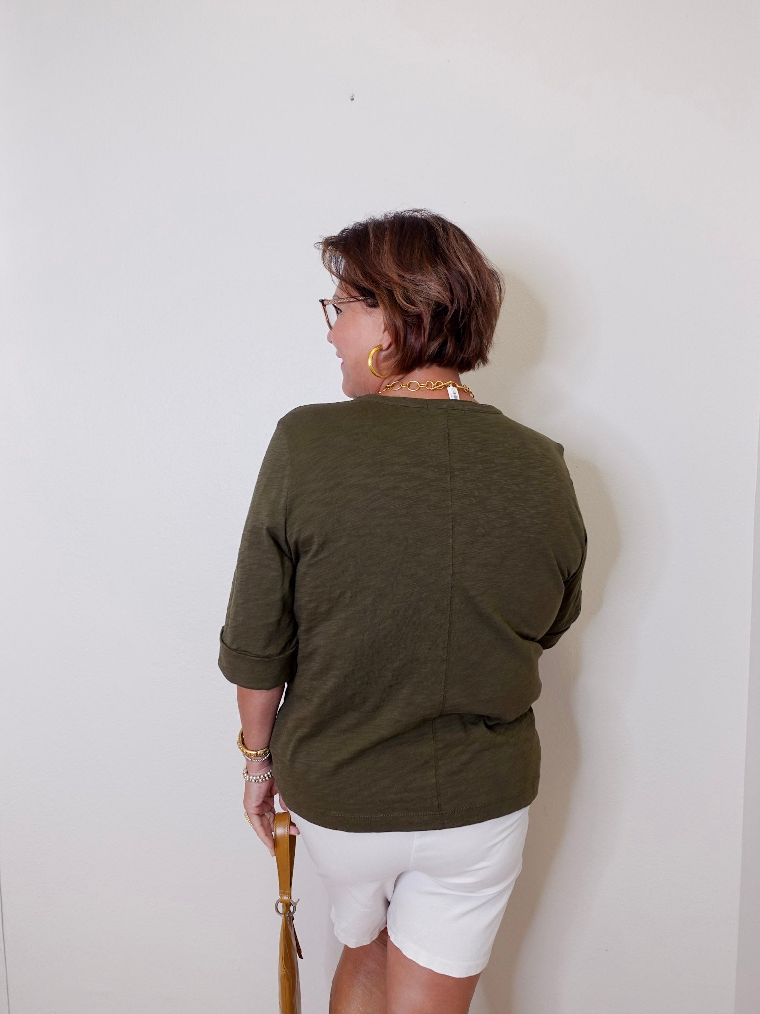 Person wearing a green shirt and white shorts against a plain wall