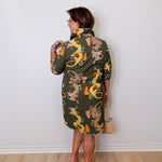 Woman wearing a patterned dress with dragons against a white wall.