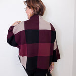Person wearing a plaid poncho against a white wall