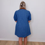 Person wearing a blue dress standing against a white wall.
