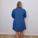 Person wearing a blue dress standing against a white wall.