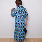 Woman wearing a blue patterned dress against a white wall.