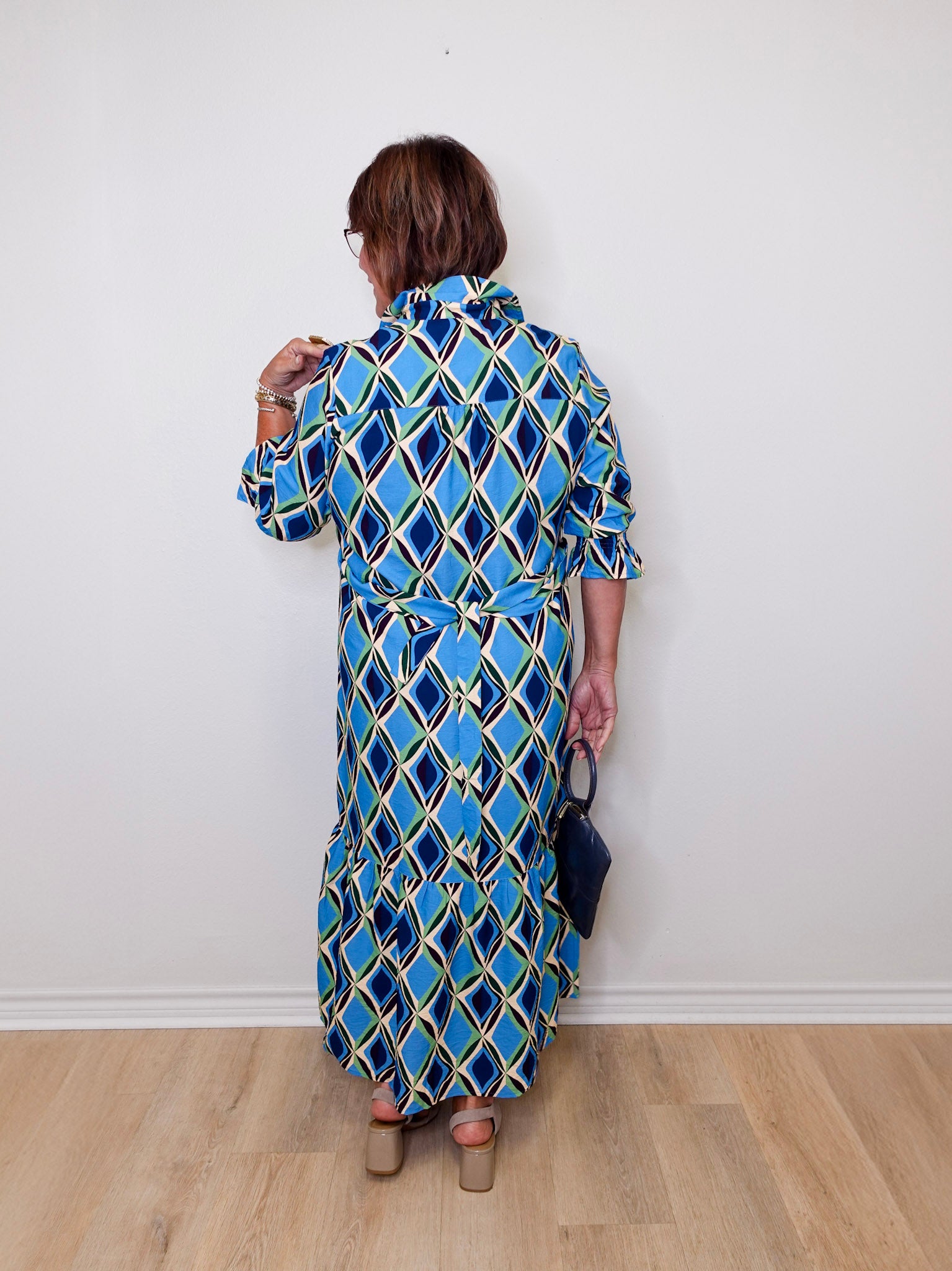 Woman wearing a blue patterned dress against a white wall.