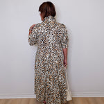 Person wearing a leopard print dress against a white wall.