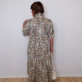 Person wearing a leopard print dress against a white wall.