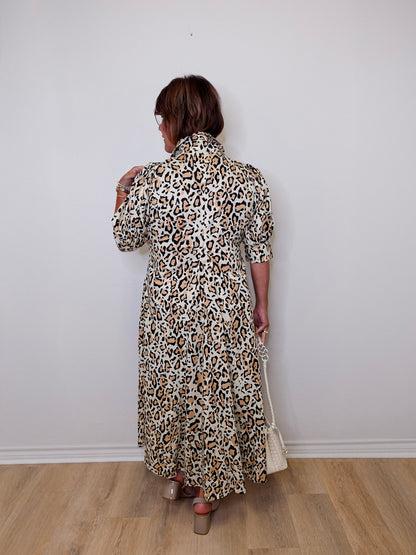 Person wearing a leopard print dress against a white wall.