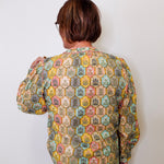 Person wearing a patterned blouse against a white wall