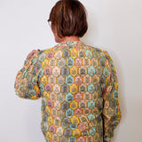 Person wearing a patterned blouse against a white wall