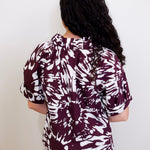 Person wearing a maroon and white patterned shirt against a plain background