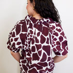 Person wearing a maroon and white patterned blouse against a plain background