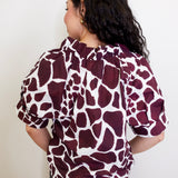 Person wearing a maroon and white patterned blouse against a plain background