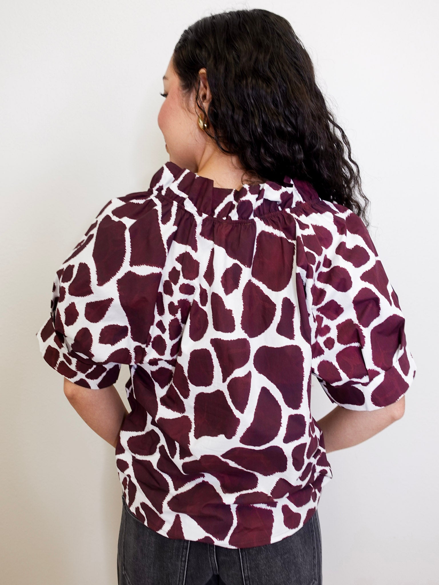Person wearing a maroon and white patterned blouse against a plain background