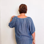 Person wearing a blue denim blouse against a white wall