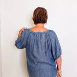 Person wearing a blue denim blouse against a white wall