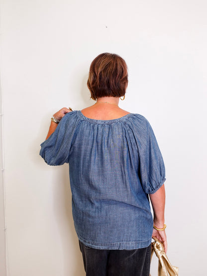 Person wearing a blue denim blouse against a white wall