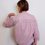 Person wearing a patterned shirt against a white wall