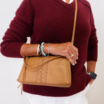 Person wearing a burgundy sweater and white pants, holding a tan leather bag.