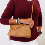 Person wearing a burgundy sweater and white pants, holding a tan leather bag.