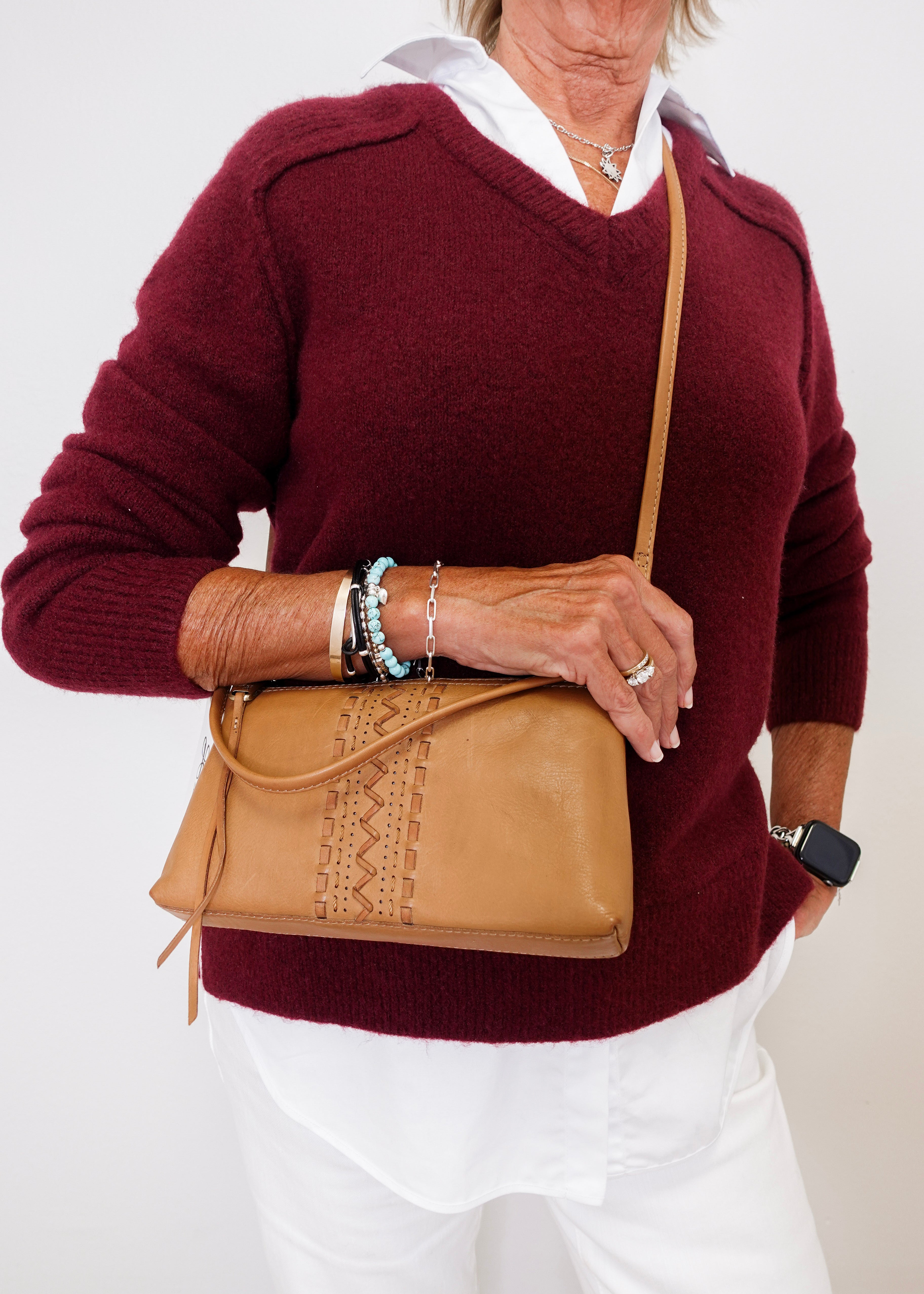 Person wearing a burgundy sweater and white pants, holding a tan leather bag.