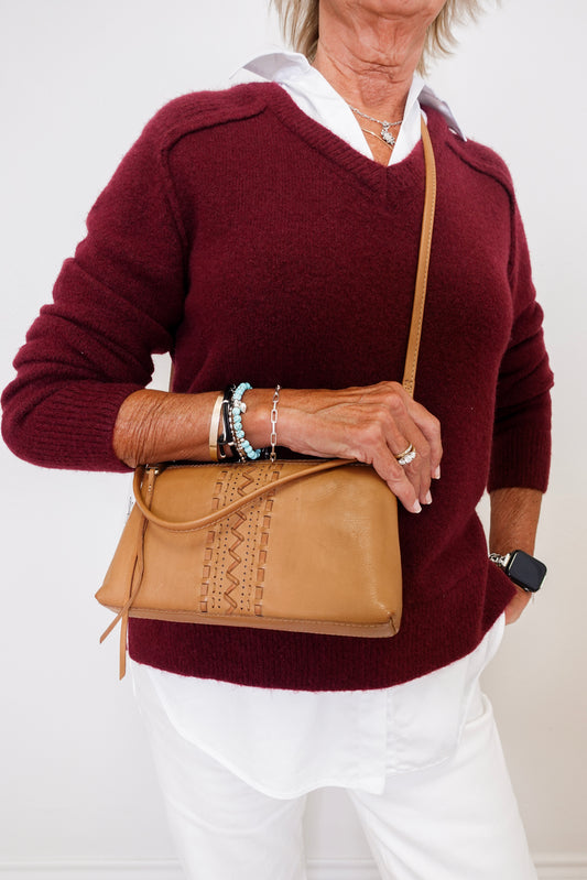 Person wearing a burgundy sweater and white pants, holding a tan leather bag.