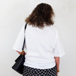 Person wearing a white t-shirt and black and white patterned pants, holding a black bag against a white background