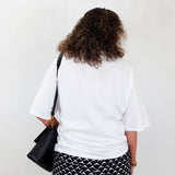Person wearing a white t-shirt and black and white patterned pants, holding a black bag against a white background