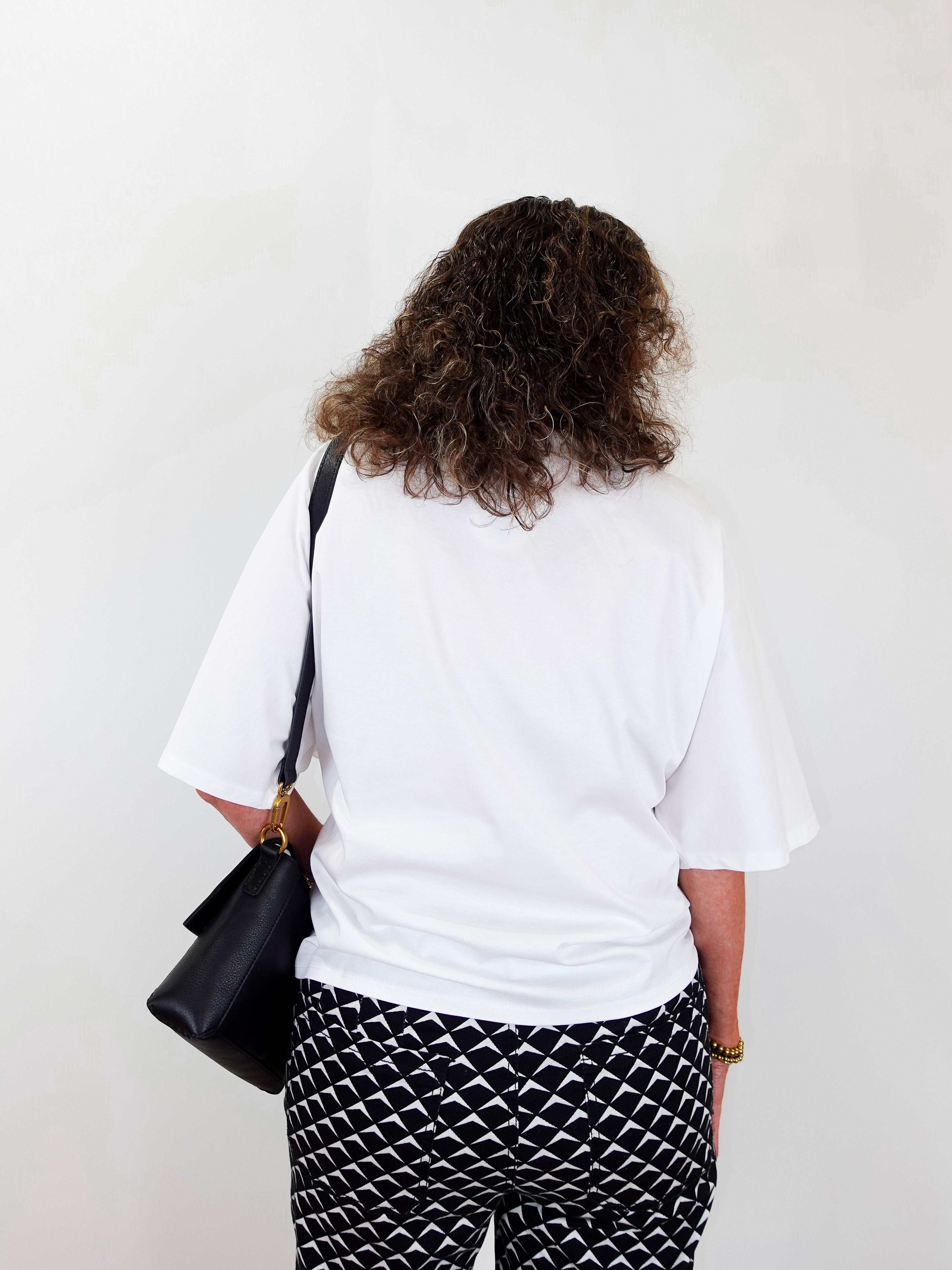 Person wearing a white t-shirt and black and white patterned pants, holding a black bag against a white background
