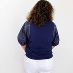 Person wearing a navy sweater with denim sleeves and white shorts on a white background