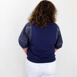 Person wearing a navy sweater with denim sleeves and white shorts on a white background