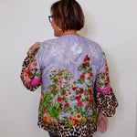 Person wearing a colorful floral and leopard print jacket against a white wall