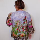 Person wearing a colorful floral and leopard print jacket against a white wall