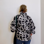 Person wearing a black and white patterned jacket against a white wall